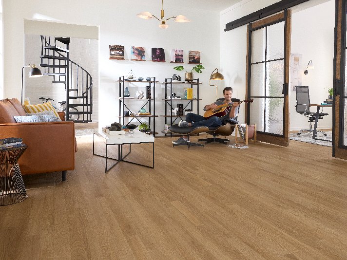 Man playing guitar and lounging in an open concept room with Pergo Flooring